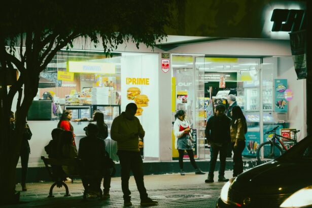 Des passants devant un magasin lumineux de nuit, discutant et utilisant leurs téléphones, créant une ambiance animée.