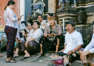 Groupe de personnes en tenue traditionnelle assises près d'un temple, discutant et utilisant des téléphones.