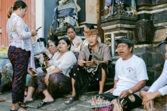 Groupe de personnes en tenue traditionnelle assises près d'un temple, discutant et utilisant des téléphones.