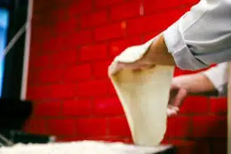 Pizzaiolo étire une pâte à pizza devant un mur de briques rouges, illustrant pourquoi les chats malaxent pour se détendre.