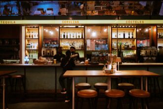 Bar animé avec des étagères de bouteilles, serveurs masqués et clients discutant. Pourquoi les chats miaulent la nuit reste un mystère.