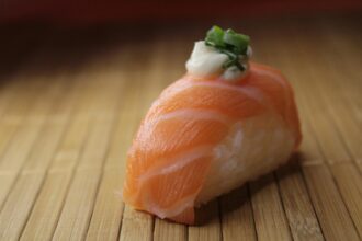 Sushi saumon sur natte de bambou, garni d'oignon vert et mayonnaise, évoque pourquoi les chats mordent par curiosité alimentaire.