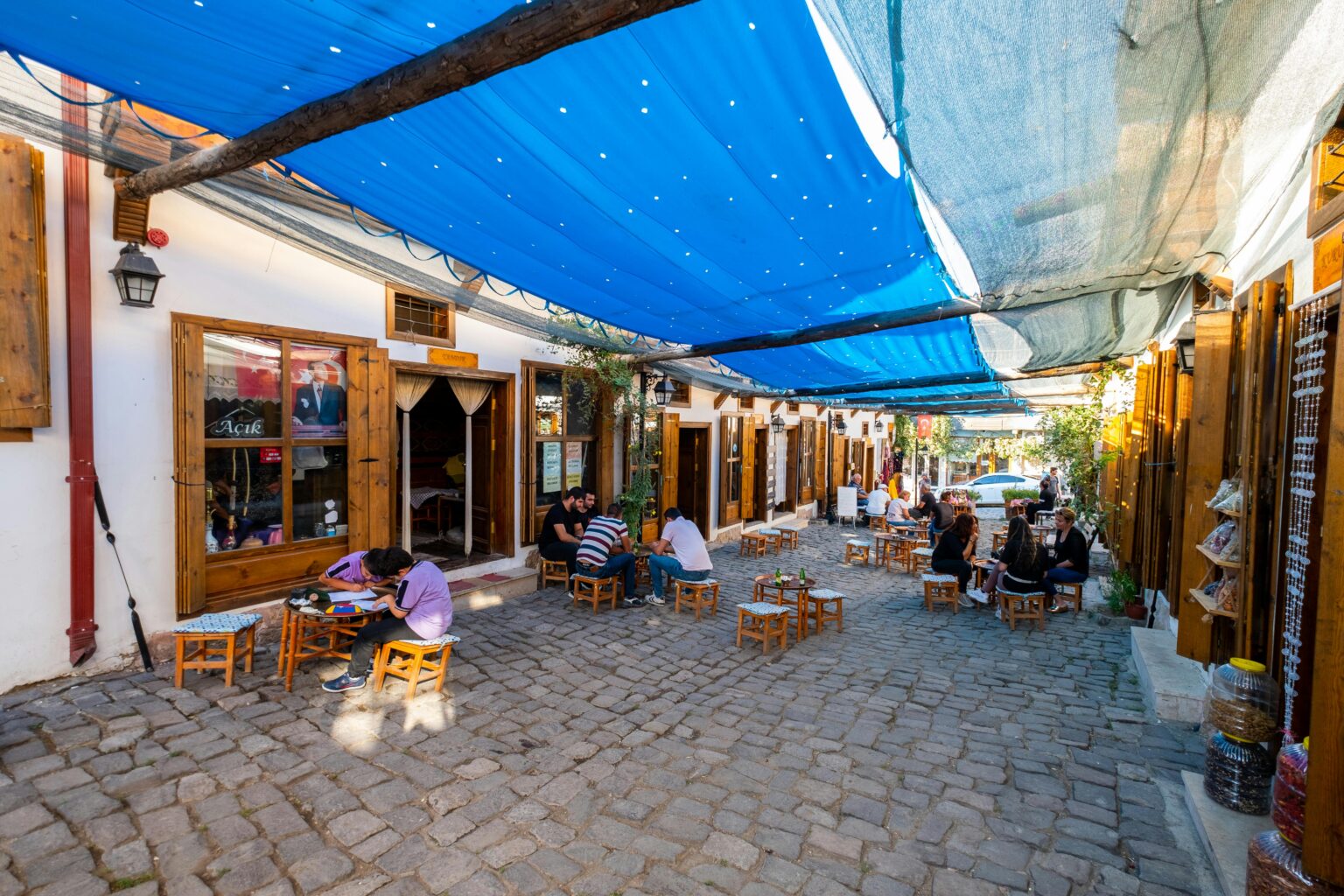 Terrasse de café animée sous un ciel bleu, des gens discutent autour de petites tables. Pourquoi les chats ronronne n'est pas évoqué ici.