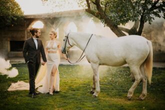 Un couple élégant pose avec un cheval blanc dans un jardin, créant une ambiance romantique et sereine.