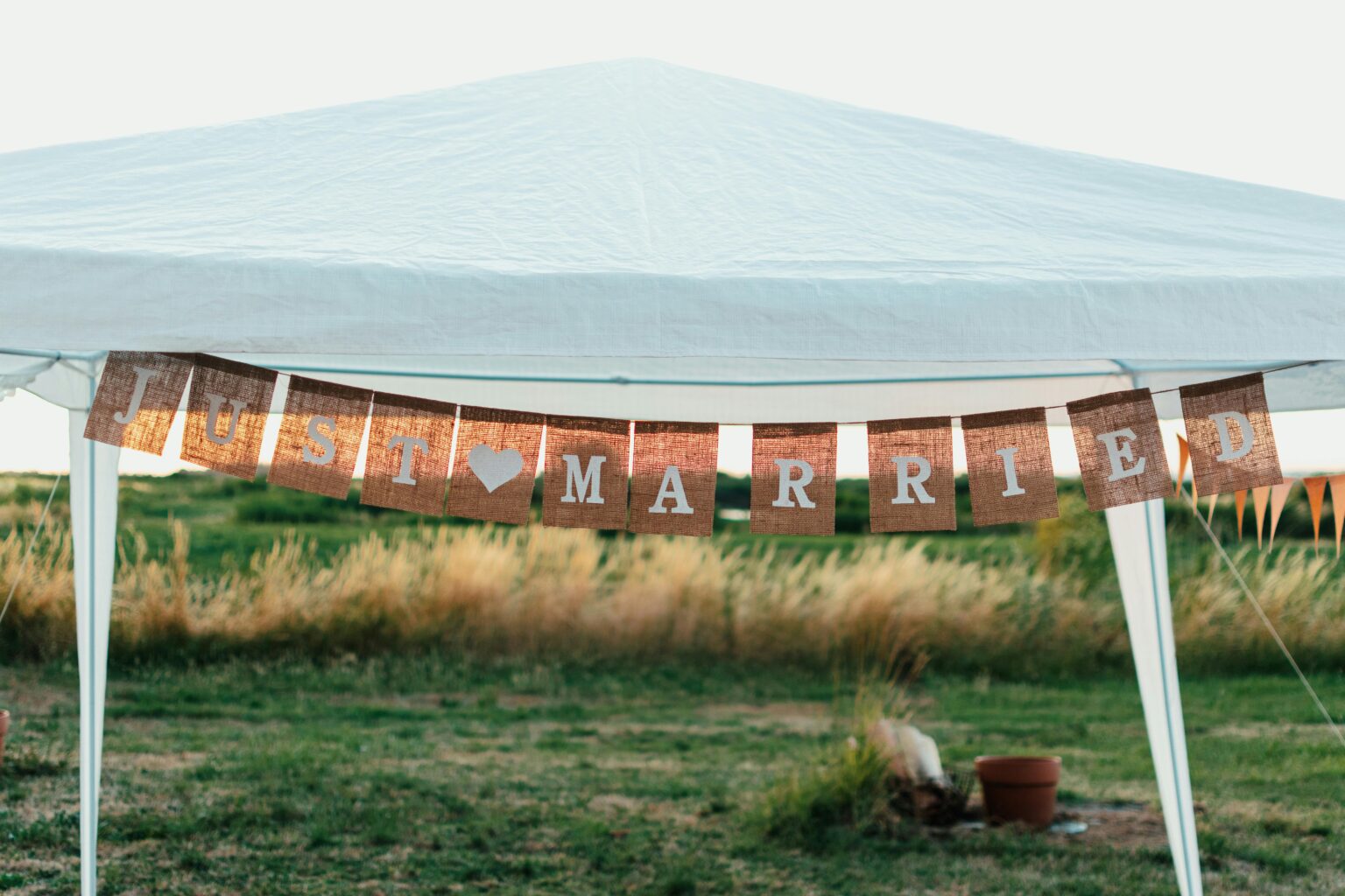 Bannière "Just Married" suspendue sous une tente blanche dans un champ, symbolisant une célébration en plein air.
