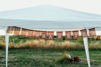 Bannière "Just Married" suspendue sous une tente blanche dans un champ, symbolisant une célébration en plein air.